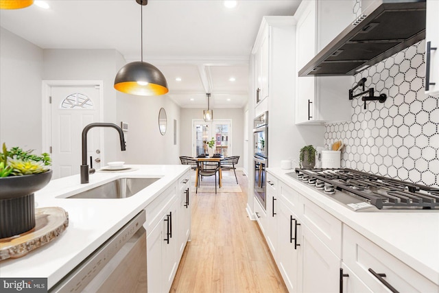 kitchen with sink, wall chimney exhaust hood, decorative light fixtures, white cabinets, and appliances with stainless steel finishes