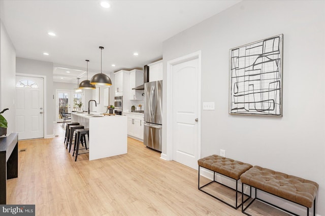 kitchen with white cabinetry, hanging light fixtures, stainless steel appliances, a breakfast bar area, and a kitchen island with sink