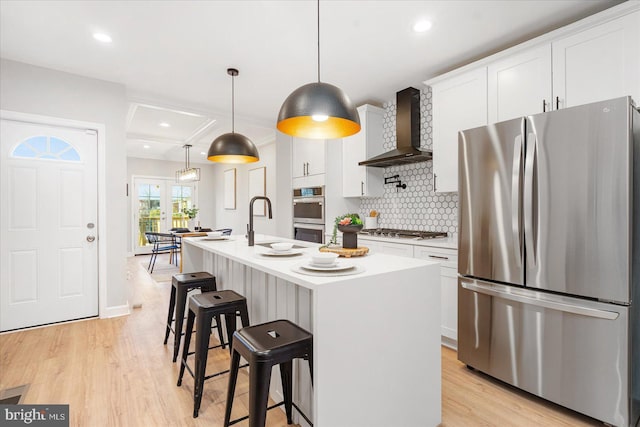 kitchen featuring white cabinetry, a center island with sink, wall chimney exhaust hood, and stainless steel appliances