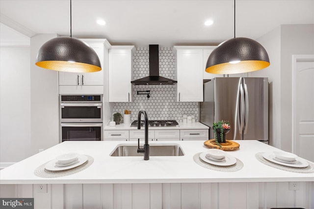 kitchen with pendant lighting, stainless steel appliances, a kitchen island with sink, and wall chimney exhaust hood