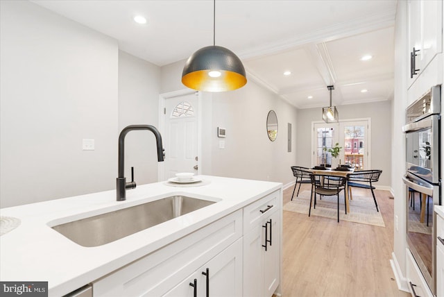 kitchen with white cabinetry, sink, decorative light fixtures, and light hardwood / wood-style flooring