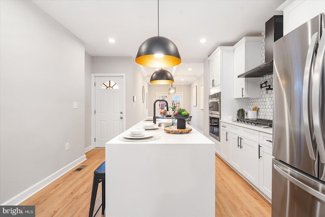 kitchen with white cabinetry, sink, decorative light fixtures, a kitchen island with sink, and appliances with stainless steel finishes