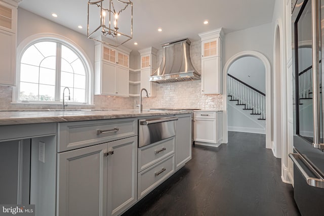 kitchen with white cabinetry, wall chimney exhaust hood, light stone counters, and decorative light fixtures