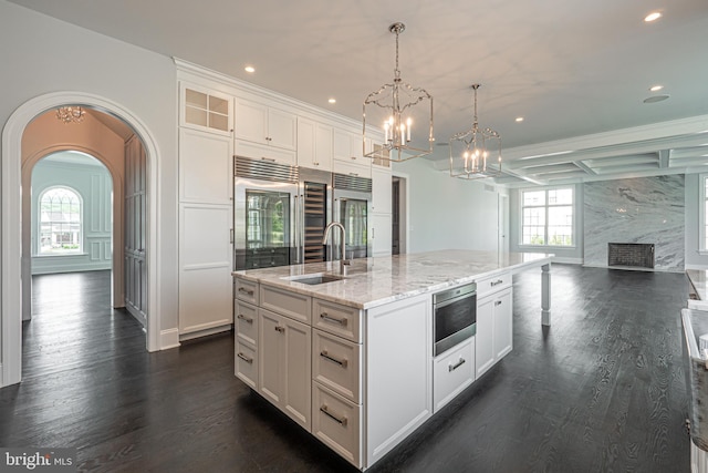 kitchen with sink, hanging light fixtures, a premium fireplace, an island with sink, and white cabinets