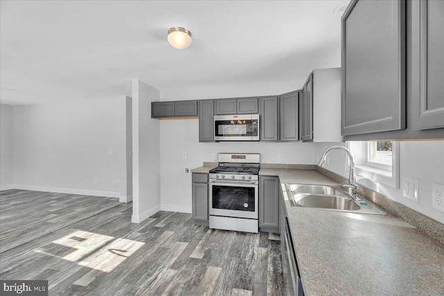 kitchen with appliances with stainless steel finishes, dark wood-type flooring, gray cabinetry, and sink