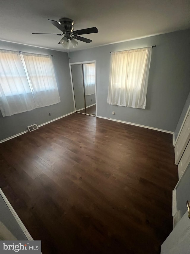 unfurnished bedroom with ceiling fan, dark wood-type flooring, and a closet