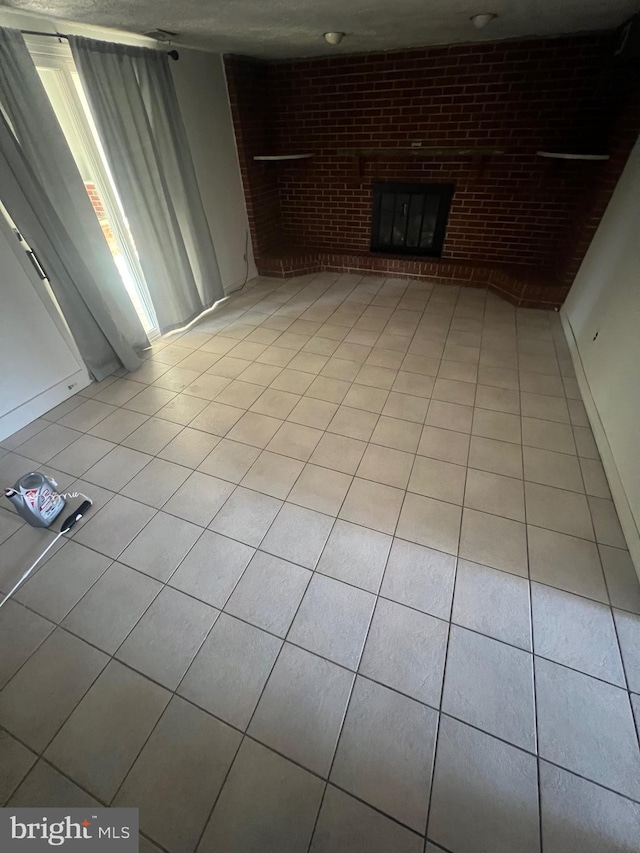 unfurnished living room with light tile patterned flooring, brick wall, and a brick fireplace