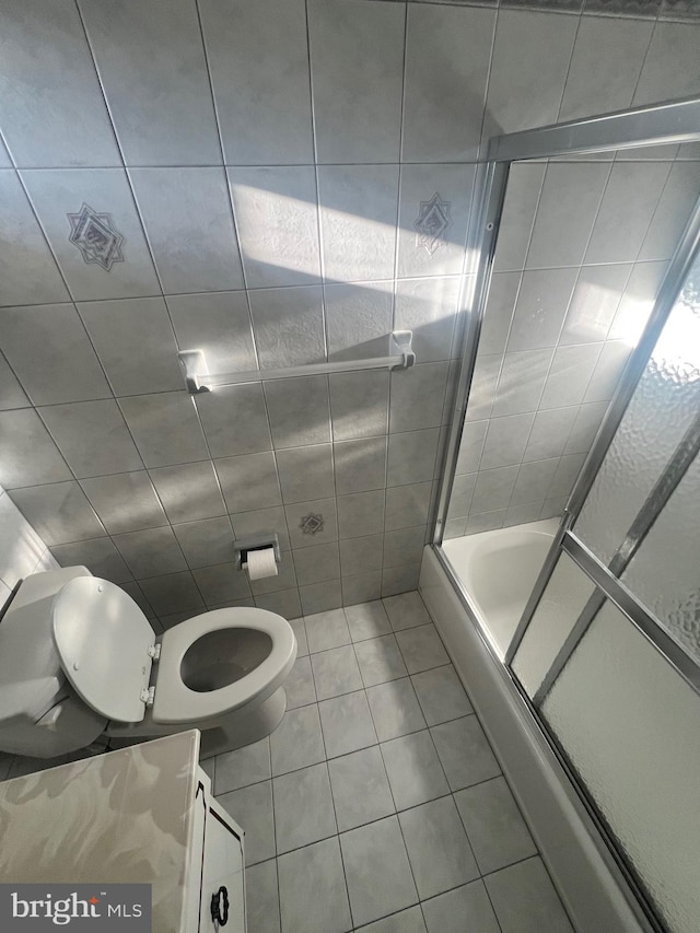 bathroom featuring tile patterned floors, shower / bath combination with glass door, tile walls, and toilet