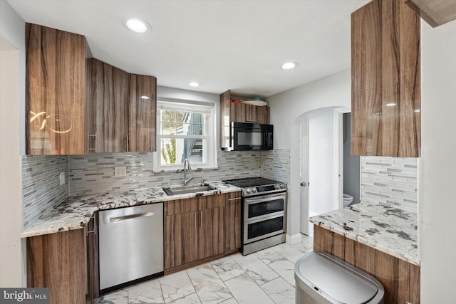 kitchen with light stone countertops, backsplash, stainless steel appliances, and sink