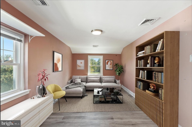 living room featuring light wood-type flooring, built in features, a wealth of natural light, and lofted ceiling