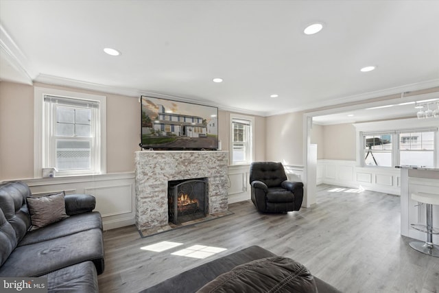 living room featuring plenty of natural light, a stone fireplace, ornamental molding, and light wood-type flooring