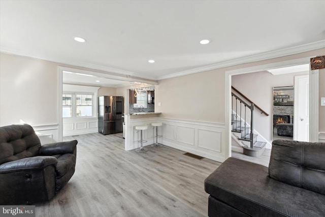 living room featuring a stone fireplace, light wood-type flooring, and crown molding