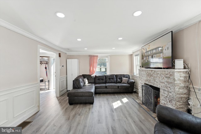 living room with a stone fireplace, crown molding, and light hardwood / wood-style flooring