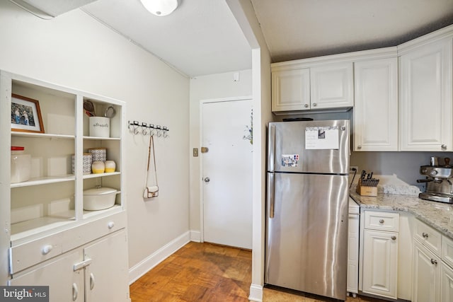 kitchen featuring light stone countertops, stainless steel fridge, and white cabinetry