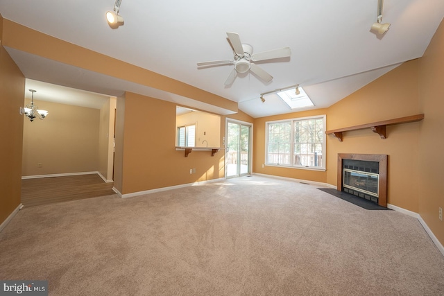 unfurnished living room featuring ceiling fan with notable chandelier, lofted ceiling with skylight, and carpet floors