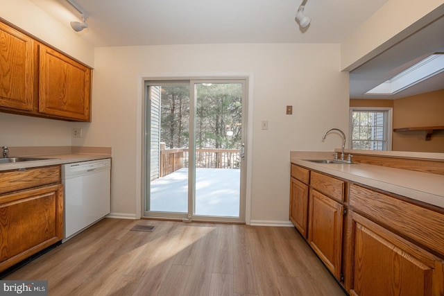 kitchen featuring white dishwasher, sink, a skylight, rail lighting, and light hardwood / wood-style floors