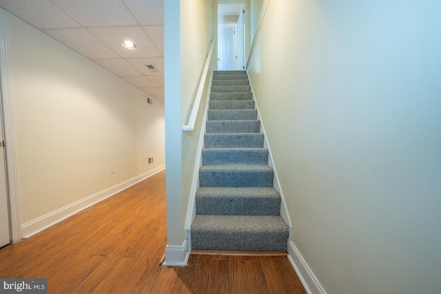 stairway featuring wood-type flooring and a drop ceiling