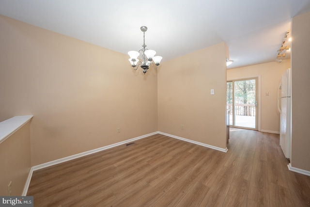 spare room with hardwood / wood-style floors and an inviting chandelier