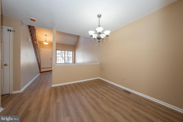 spare room with vaulted ceiling, hardwood / wood-style floors, and an inviting chandelier