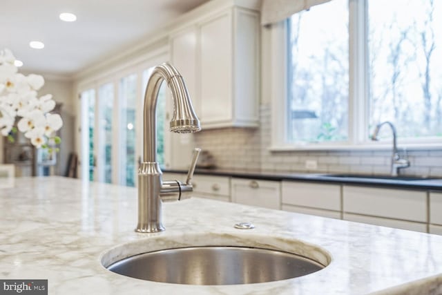 room details with white cabinets, decorative backsplash, dark stone countertops, and sink