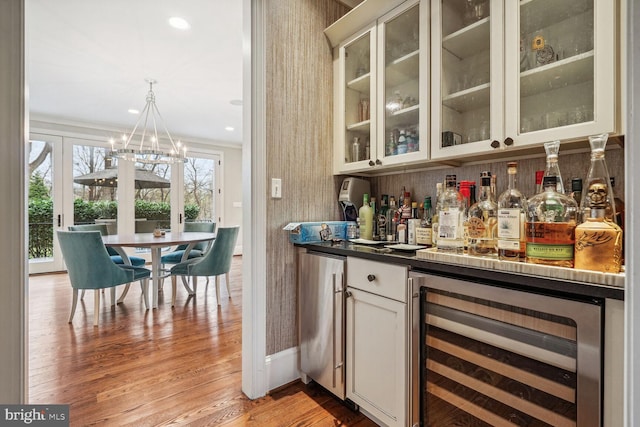 bar with light wood-type flooring, refrigerator, crown molding, white cabinets, and wine cooler