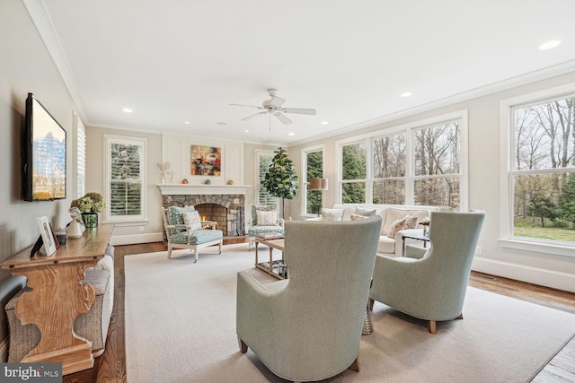 living room with hardwood / wood-style floors, a stone fireplace, ceiling fan, and ornamental molding