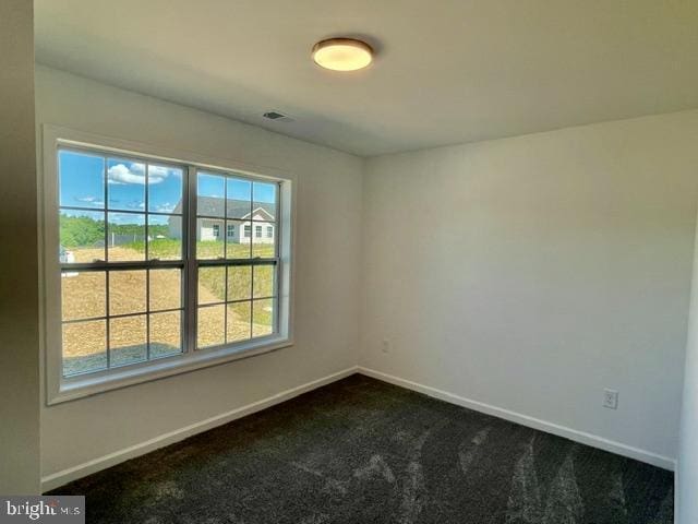 spare room with a healthy amount of sunlight and dark colored carpet