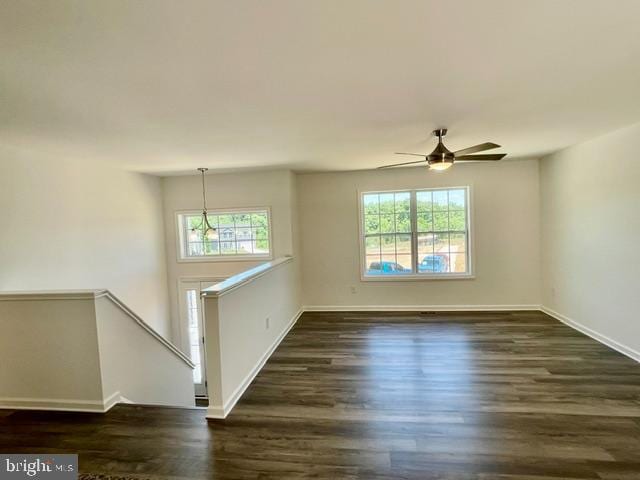 empty room featuring ceiling fan with notable chandelier and dark wood-type flooring