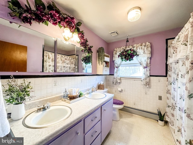 bathroom featuring a baseboard heating unit, visible vents, a sink, and tile walls