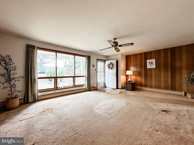 carpeted empty room featuring a ceiling fan, a baseboard radiator, and wood walls