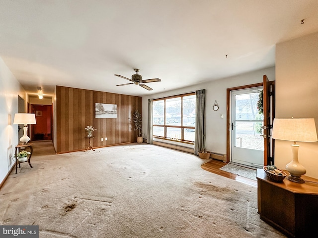 unfurnished living room featuring carpet floors, a baseboard radiator, wood walls, ceiling fan, and baseboards