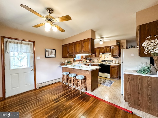 kitchen with electric stove, a breakfast bar area, a baseboard heating unit, under cabinet range hood, and a peninsula