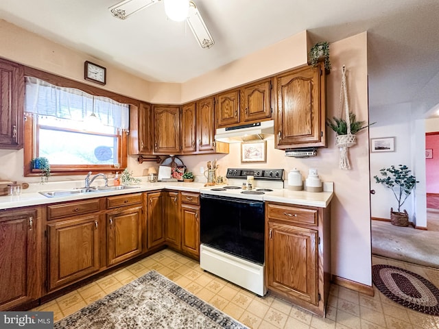 kitchen with light countertops, electric range oven, brown cabinetry, a sink, and under cabinet range hood