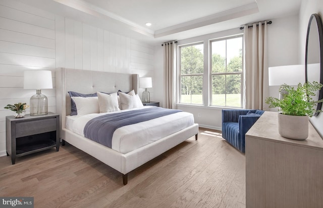 bedroom with crown molding, light hardwood / wood-style flooring, wooden walls, and a tray ceiling