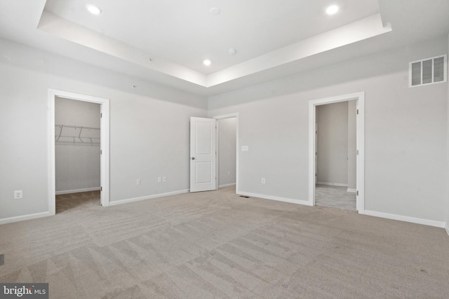 unfurnished bedroom featuring a closet, light colored carpet, a walk in closet, and a tray ceiling