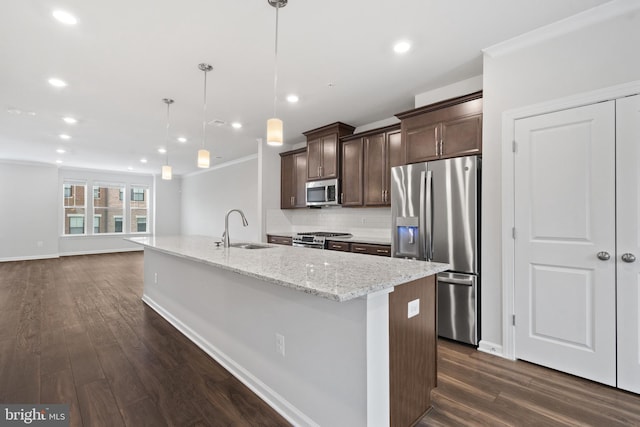 kitchen featuring light stone countertops, sink, hanging light fixtures, stainless steel appliances, and an island with sink