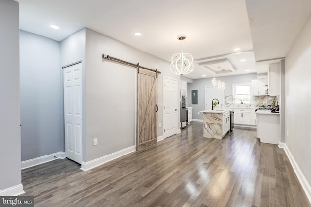 kitchen featuring dark wood-type flooring, a center island with sink, light countertops, a barn door, and white cabinetry