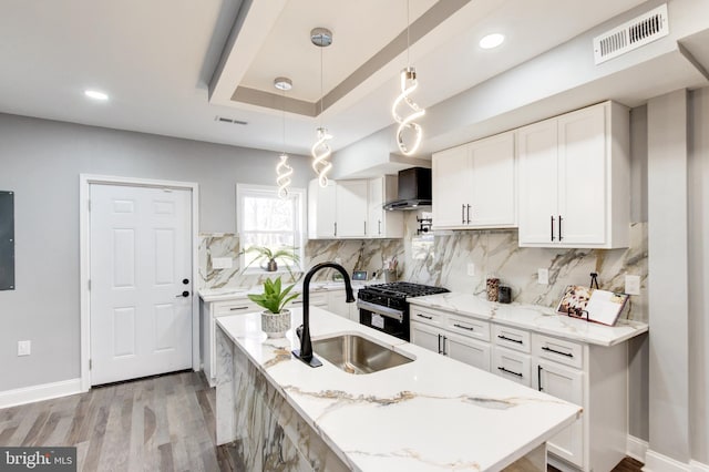 kitchen with visible vents, a sink, gas stove, wall chimney exhaust hood, and a raised ceiling