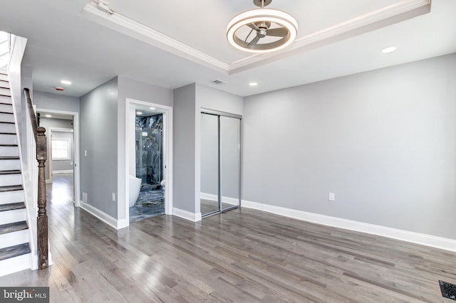 unfurnished bedroom featuring visible vents, a tray ceiling, wood finished floors, crown molding, and baseboards