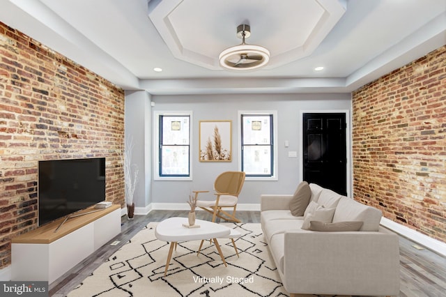 living room with baseboards, brick wall, light wood-style flooring, recessed lighting, and a raised ceiling