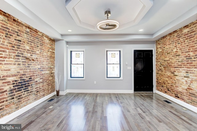 foyer entrance featuring a tray ceiling, wood finished floors, and brick wall