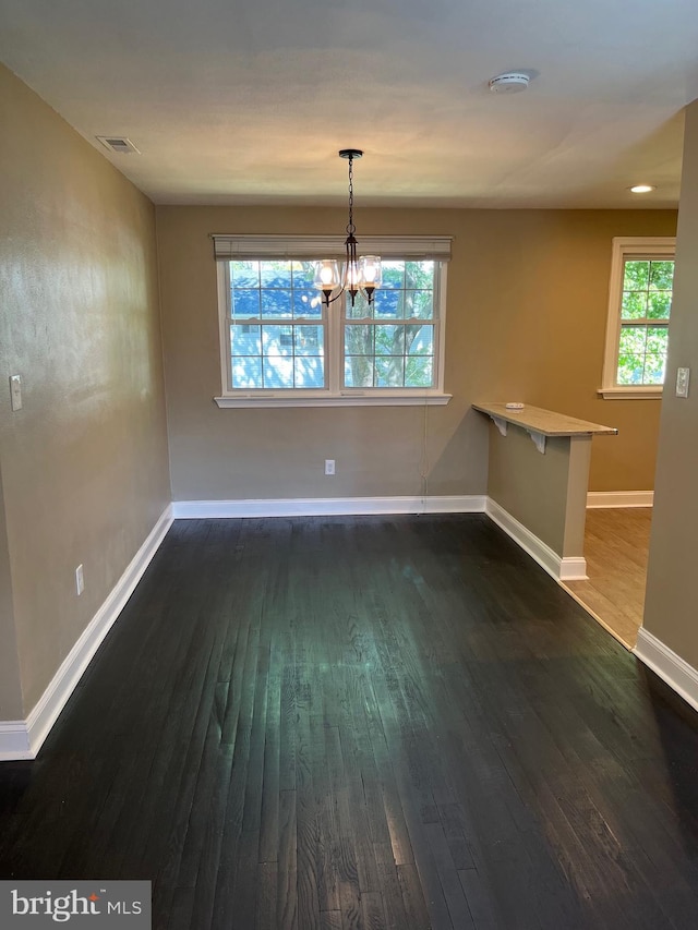 unfurnished dining area featuring a chandelier, plenty of natural light, and dark wood-type flooring