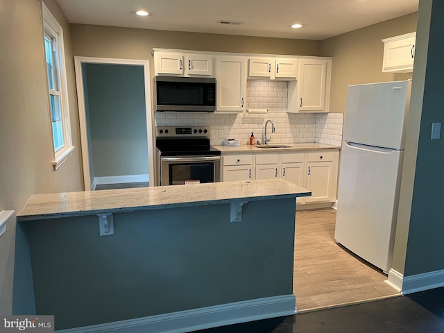 kitchen with sink, light stone countertops, appliances with stainless steel finishes, white cabinetry, and a breakfast bar area