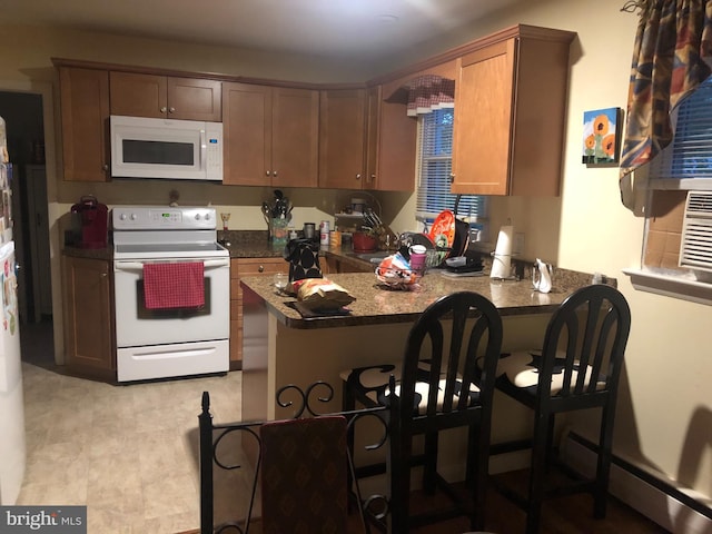 kitchen with kitchen peninsula, dark stone counters, white appliances, a baseboard heating unit, and a breakfast bar area