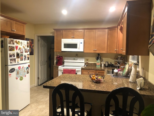 kitchen with white appliances, kitchen peninsula, and dark stone counters