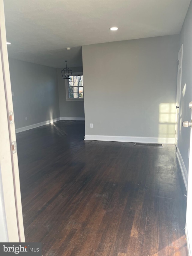 spare room with dark wood-type flooring and an inviting chandelier