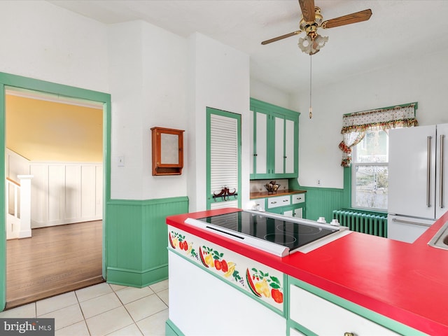 kitchen with radiator, black electric stovetop, white refrigerator, ceiling fan, and light tile patterned floors