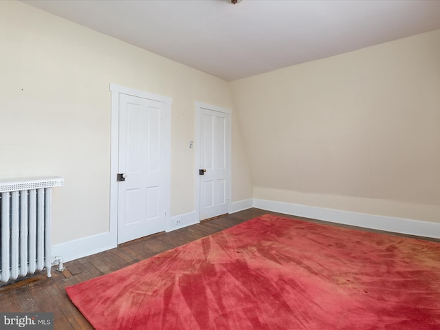 empty room with radiator heating unit and dark hardwood / wood-style flooring