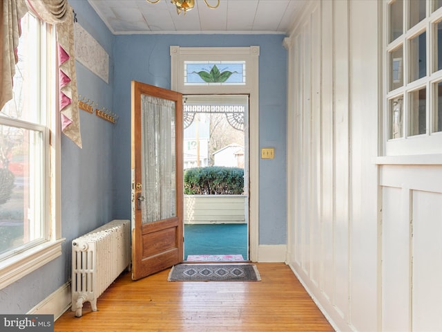 foyer with radiator heating unit, light hardwood / wood-style floors, a notable chandelier, and ornamental molding