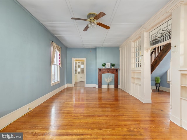 unfurnished living room featuring built in shelves, ceiling fan, and light wood-type flooring